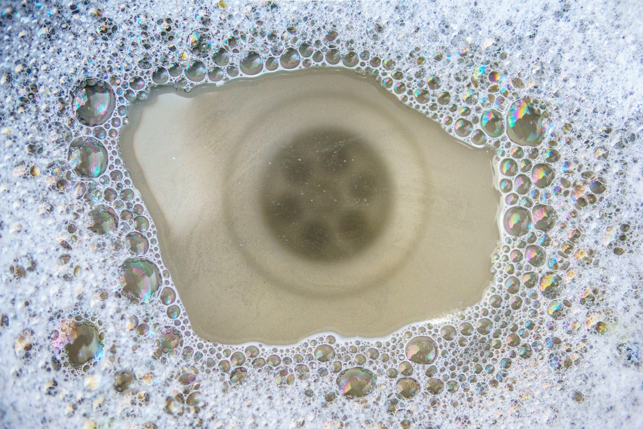 An image looking down at a kitchen sink that has standing water and some soap bubbles in it.