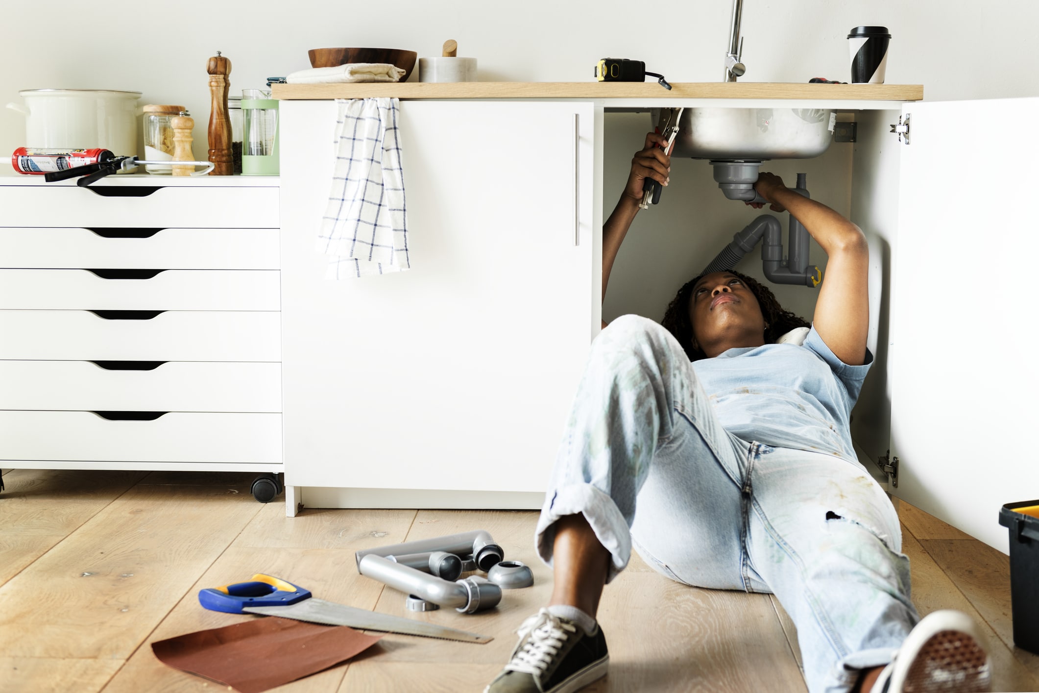 A female homeowner laying under her bathroom sink fixing it.